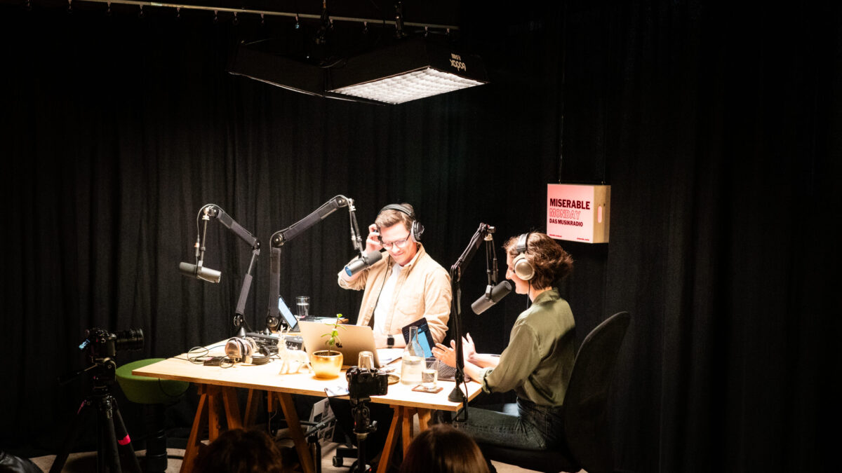 Ein Mann und eine Frau mit Kopfhörern zwischen Mikros in einem Aufnahmestudio