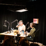 Ein Mann und eine Frau mit Kopfhörern zwischen Mikros in einem Aufnahmestudio