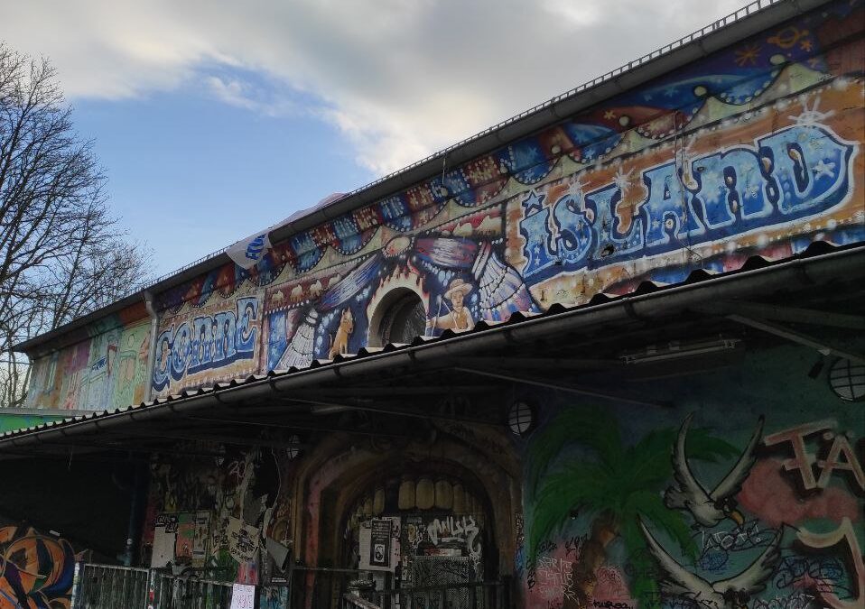 Die Fassade des Clubs Conne Island mit vielen Graffittis, im Hintergrund blauer Himmel und weiße Wolken.