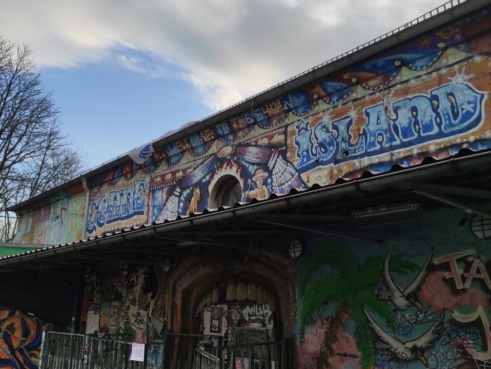 Die Fassade des Clubs Conne Island mit vielen Graffittis, im Hintergrund blauer Himmel und weiße Wolken.