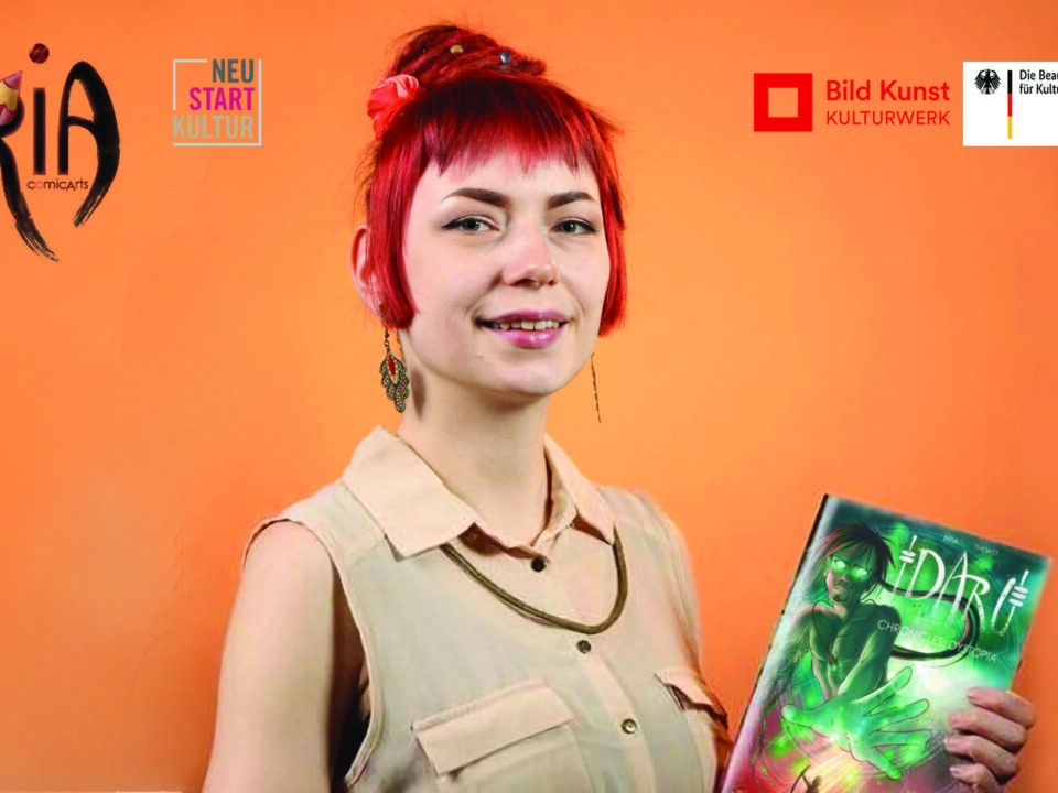 Eine weiße Frau mit knallrot gefärbten Haaren vor orangenem Hintergrund. Sie trägt ein Comic in den Händen mit der Aufschrift Daru.