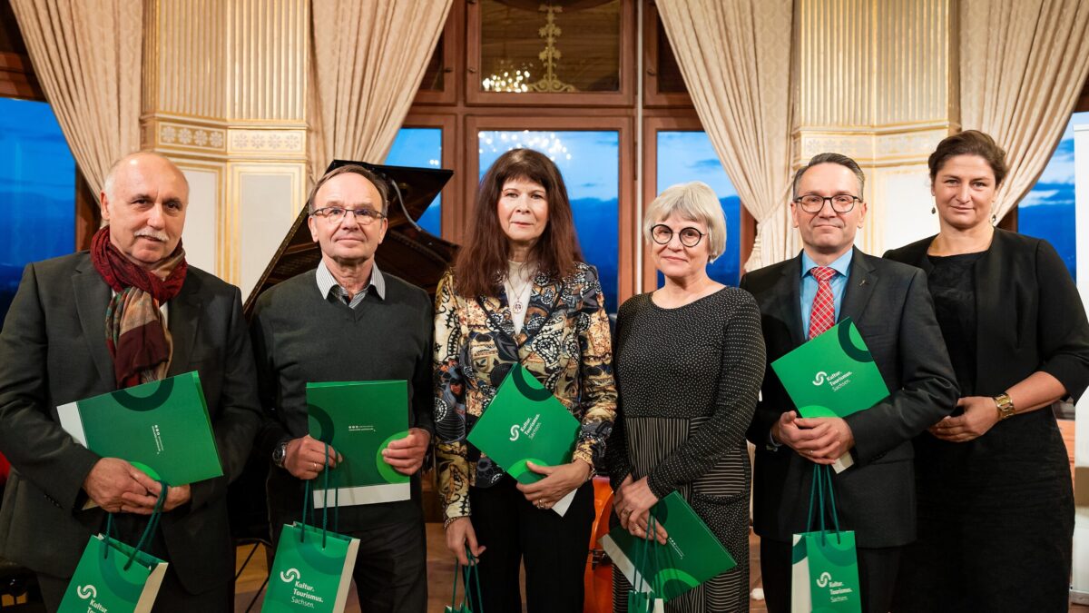 Sechs weiße Personen, drei Frauen, drei Männer, alle schick gekleidet. Fünf Menschen halten eine grüne Urkunde und grüne Taschen in der Hand mit der Aufschrift: Kultur Tourismus Sachsen.