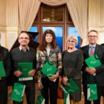 Sechs weiße Personen, drei Frauen, drei Männer, alle schick gekleidet. Fünf Menschen halten eine grüne Urkunde und grüne Taschen in der Hand mit der Aufschrift: Kultur Tourismus Sachsen.