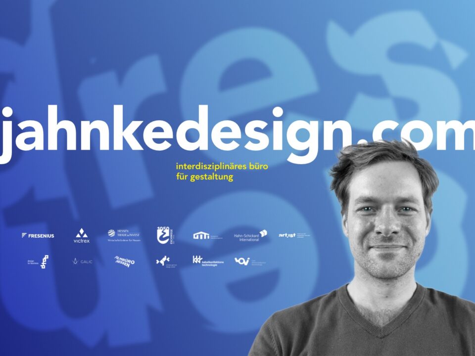 Ein weißer junger Mann lächelt in die Kamera, sein Foto ist schwarz-weiß gehalten. Der Hintergrund ist blau mit der Aufschrift: jahnkedesign.com