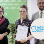 Drei weiße Personen, zwei Frauen links, ein Mann rechts. Die Frau in der Mitte trägt Blumen und enie Urkunde in der Hand. Aufschrift: Sächsischer Verlagspreis 22