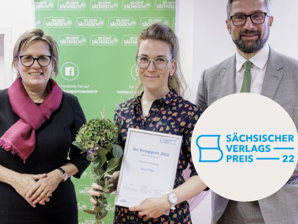 Drei weiße Personen, zwei Frauen links, ein Mann rechts. Die Frau in der Mitte trägt Blumen und enie Urkunde in der Hand. Aufschrift: Sächsischer Verlagspreis 22
