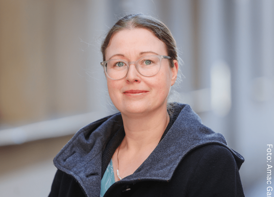 Weiße Frau mit Brille und zusammengebundenen haaren, sie trägt eine dunkleJacke