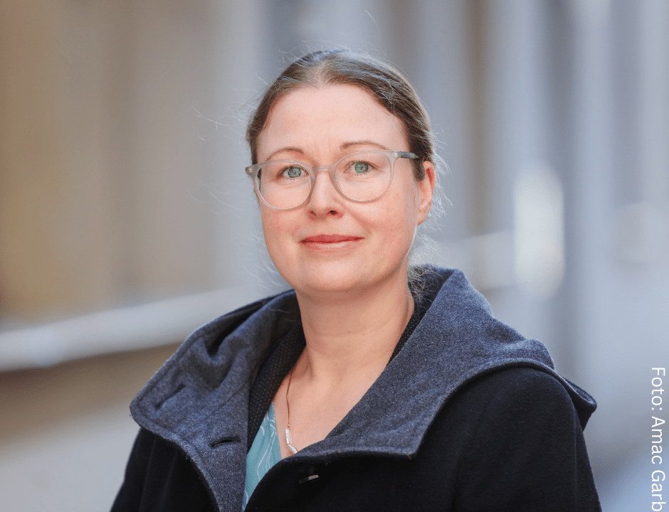 Weiße Frau mit Brille und zusammengebundenen haaren, sie trägt eine dunkleJacke